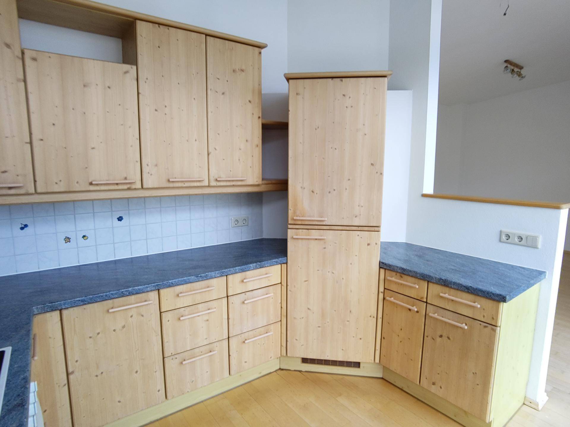 Geräumige Küche mit vielen Holzschränken und dunkler Arbeitsplatte.