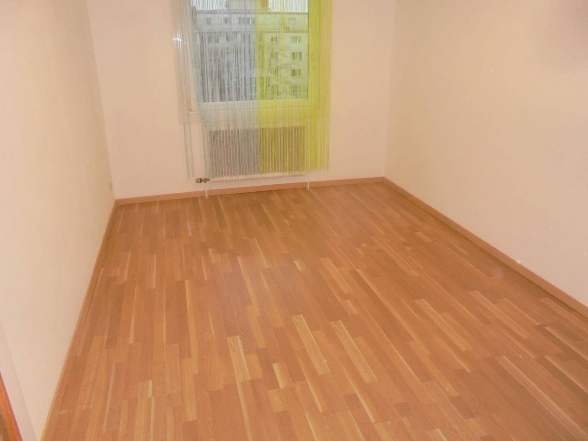 Leeres Zimmer mit hellem Parkettboden und Fenster mit Blick nach draußen.