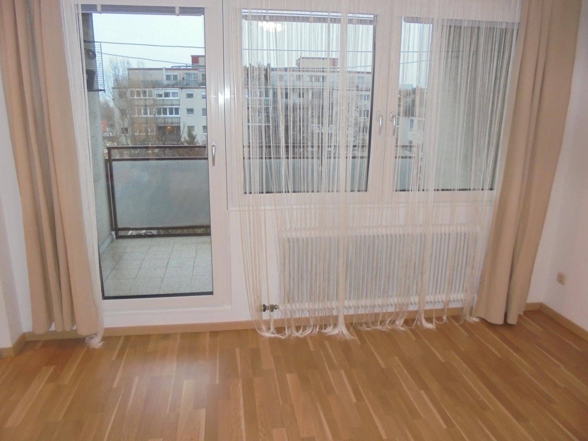 Heller Raum mit Parkettboden und Zugang zu einem kleinen Balkon.