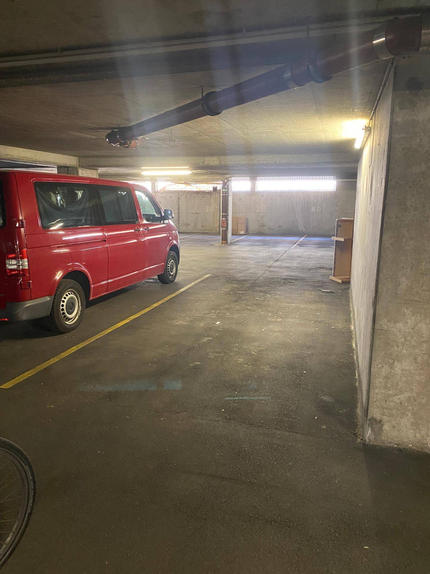 Tiefgarage mit einem geparkten roten Lieferwagen, sichtbaren Rohren an der Decke und Tageslichteinfall.
