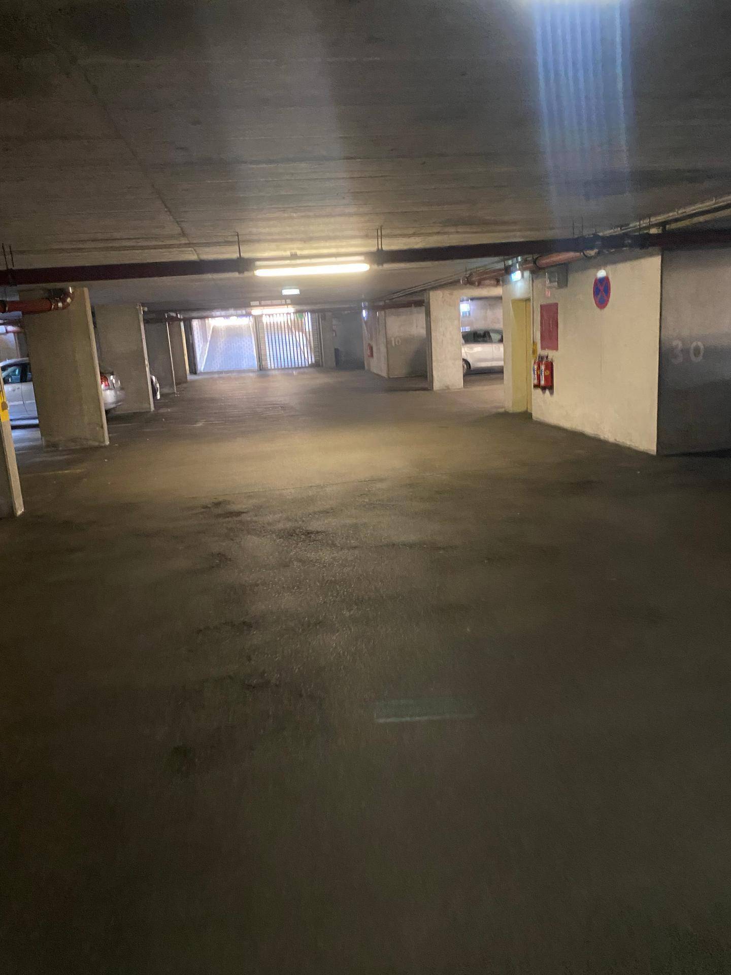 Weitläufige Tiefgarage mit vielen freien Stellplätzen, Betonpfeilern und sichtbarem Ausgangsbereich.