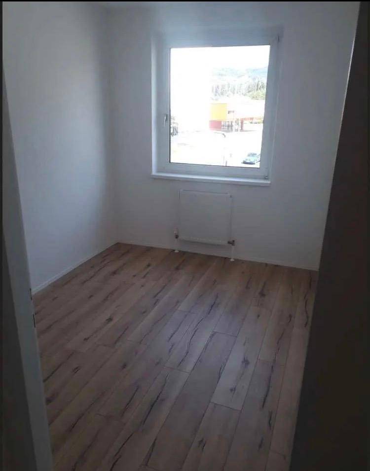 Leeres Zimmer mit Holzfußboden und einem großen Fenster, das viel Tageslicht hereinlässt.