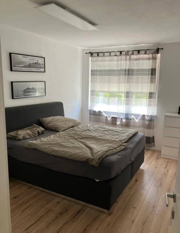 Schlafzimmer mit Doppelbett, Holzfußboden und einem Fenster mit Vorhängen.