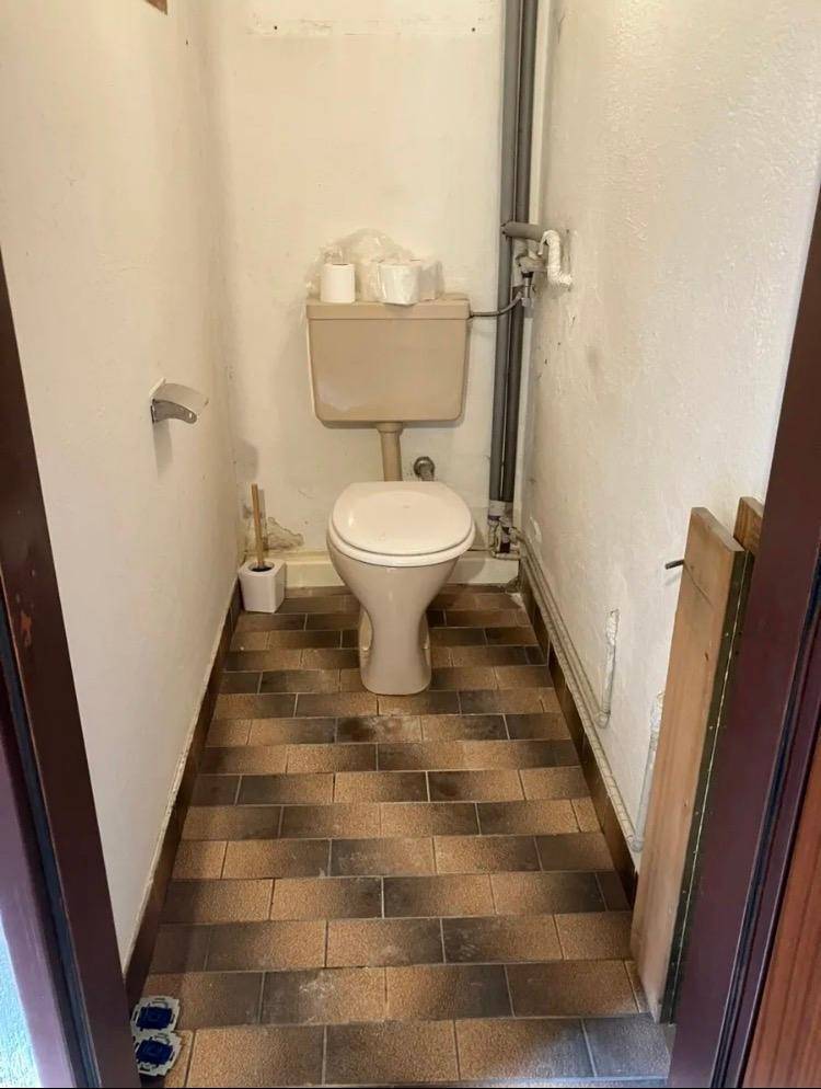 Kleines Gäste-WC mit einfacher Toilette und braun-beigen Fliesen, funktional und sauber.