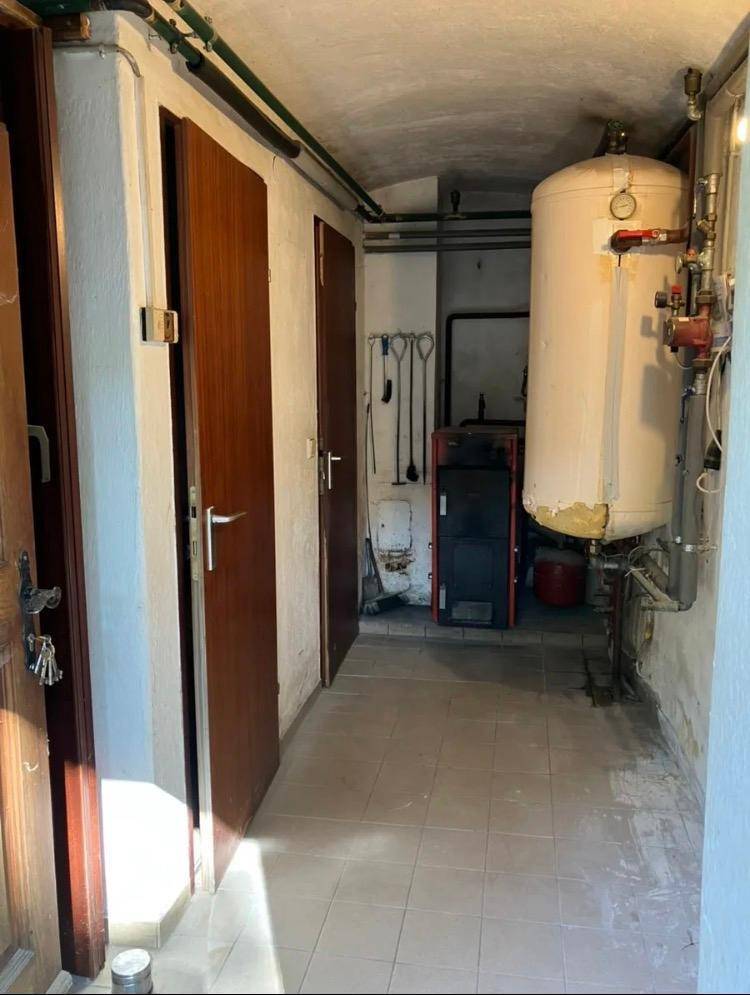 Heizungsraum im Keller mit Warmwasserspeicher und Heizkessel, umgeben von Türen und Leitungen.