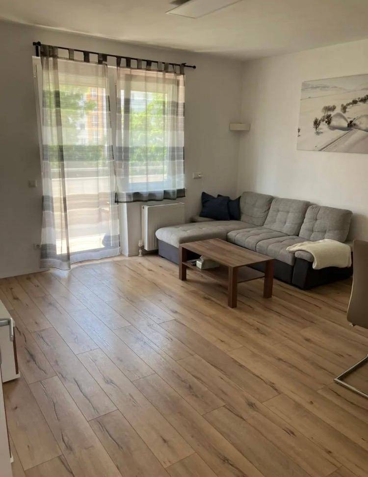 Gemütliches Wohnzimmer mit großem Ecksofa, Holzboden und Zugang zu einem Balkon.