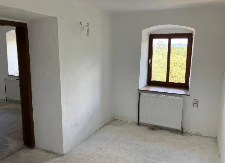 Heller Raum mit einem Fenster, Heizkörper und unfertigem Betonboden, der auf eine Renovierung wartet.