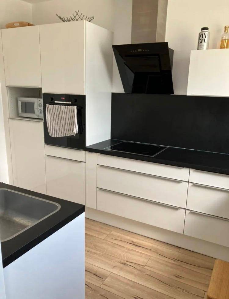 Moderne Küche mit weißen Hochglanzfronten, schwarzer Arbeitsplatte und integrierten Elektrogeräten.