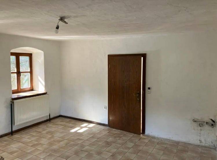 Heller Raum mit beigefarbenen Fliesen und einer Holztür, die auf eine Renovierung wartet.