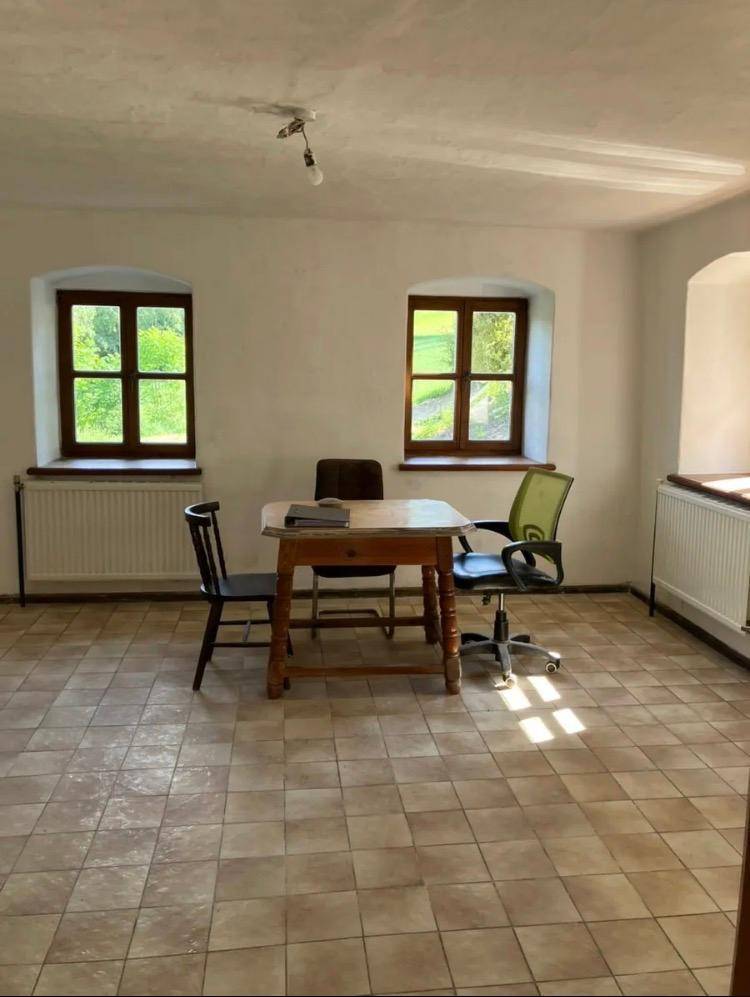 Geräumiger Raum mit beigefarbenen Fliesen, einem Holztisch und Stühlen, ideal als Büro oder Esszimmer.