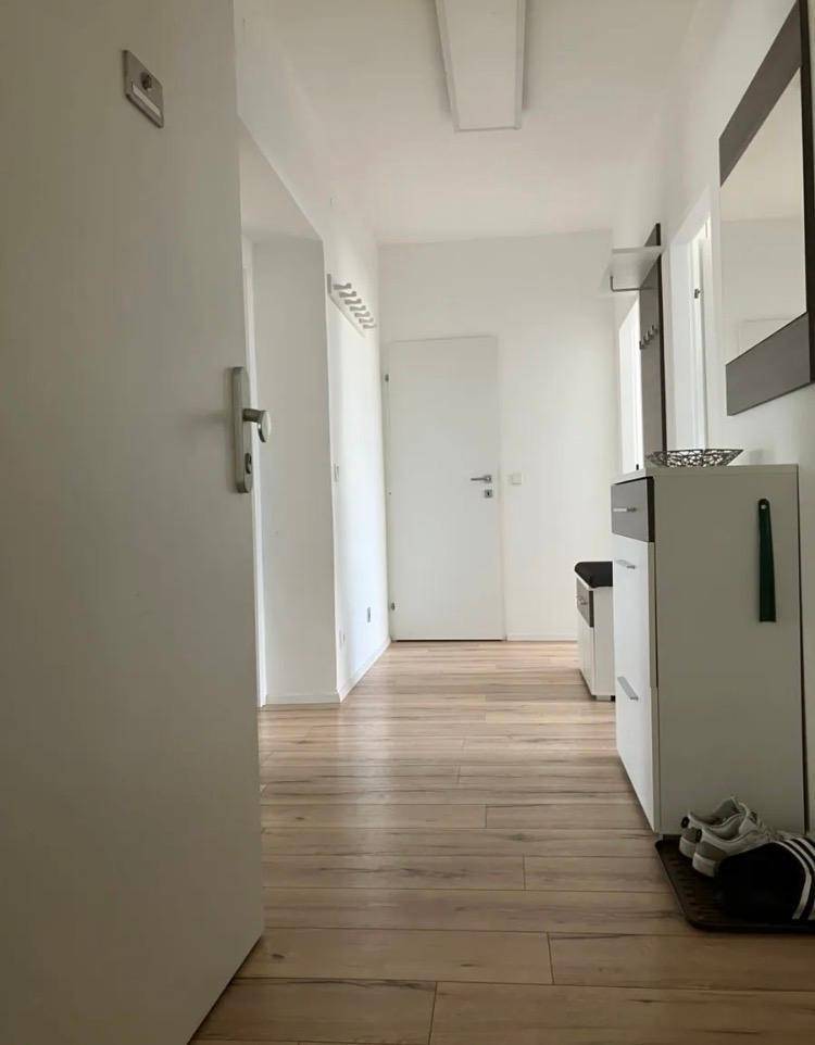 Heller Flur mit Holzfußboden, weiß gestrichenen Wänden und einem modernen Schuhschrank.