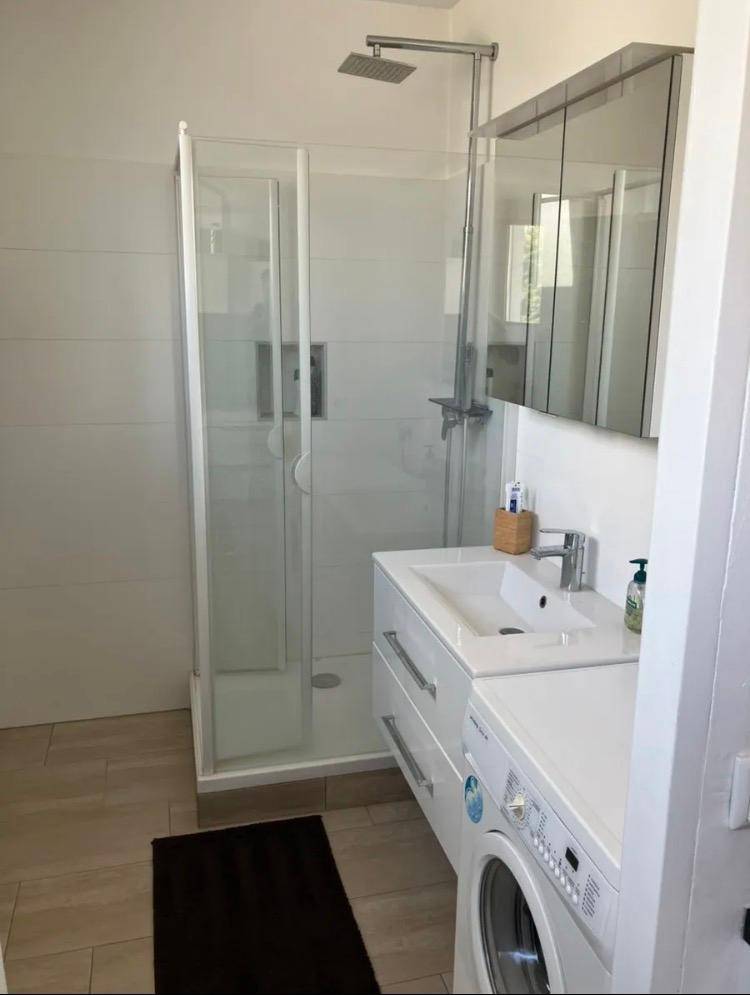 Modernes Badezimmer mit Duschkabine, Waschbecken und integrierter Waschmaschine.