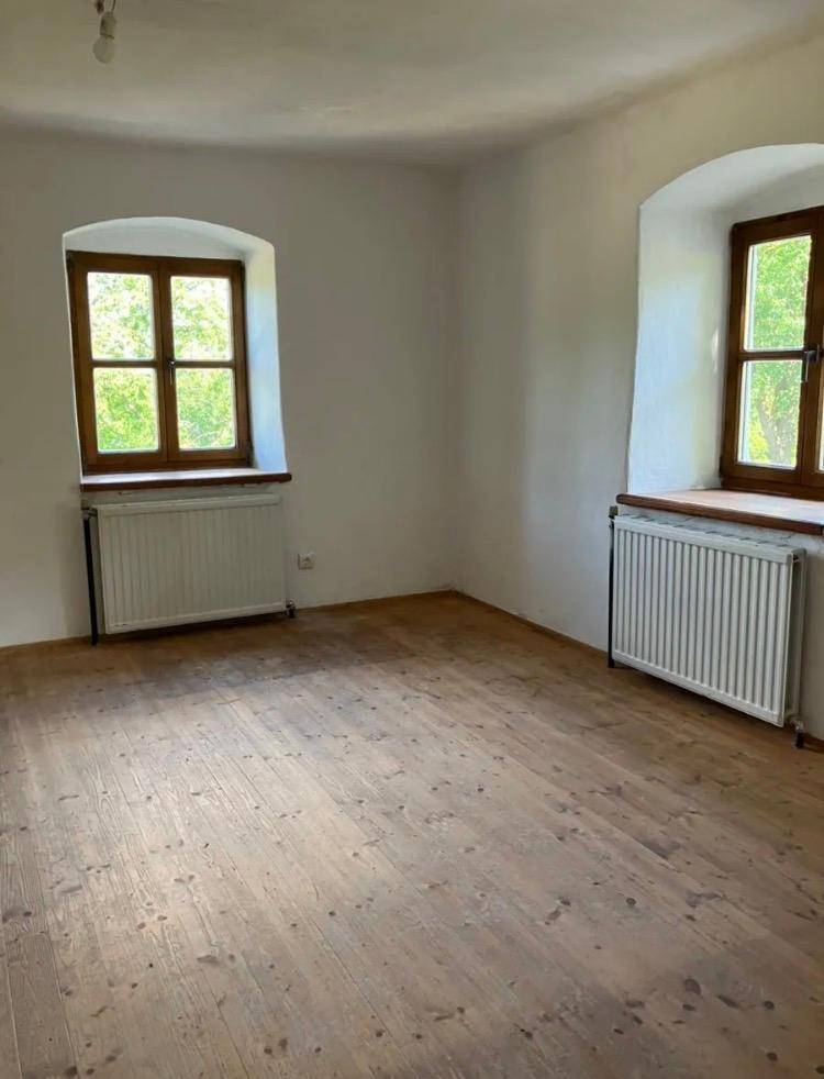 Heller Raum mit zwei Fenstern und abgenutztem Holzboden, der viel Potenzial bietet.