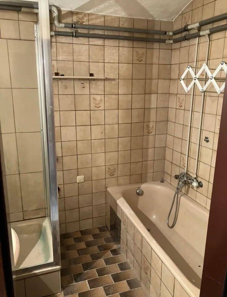 Badezimmer mit Badewanne, Duschkabine und beigefarbenen Fliesen, in einem älteren Stil.