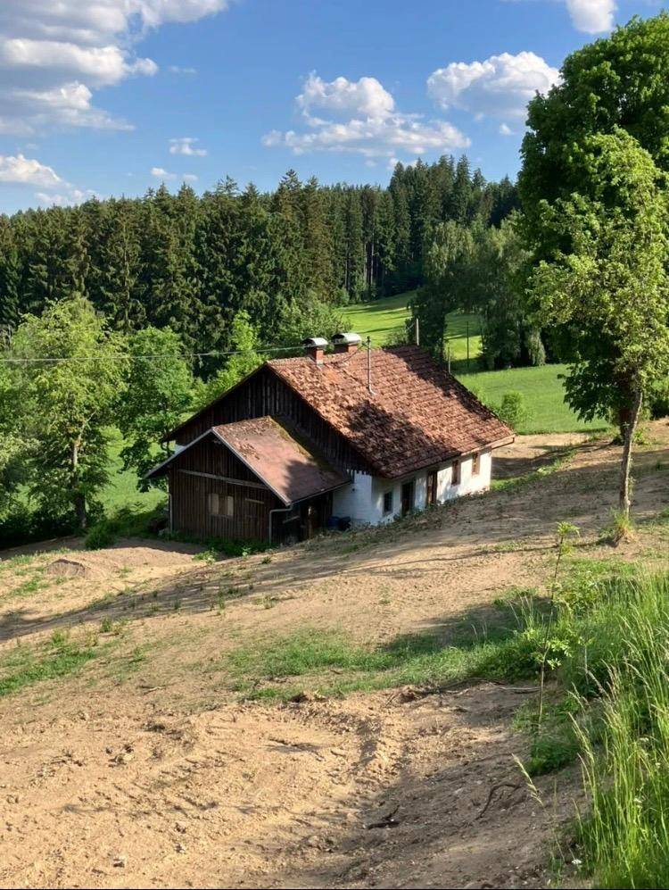 Nähere Ansicht des ländlichen Hauses mit Ziegeldach und angrenzendem Holzschuppen in sonniger Umgebung.
