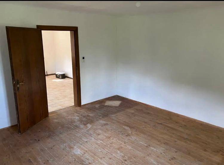 Leerer Raum mit Holztür und abgenutztem Holzboden, der auf eine Renovierung wartet.