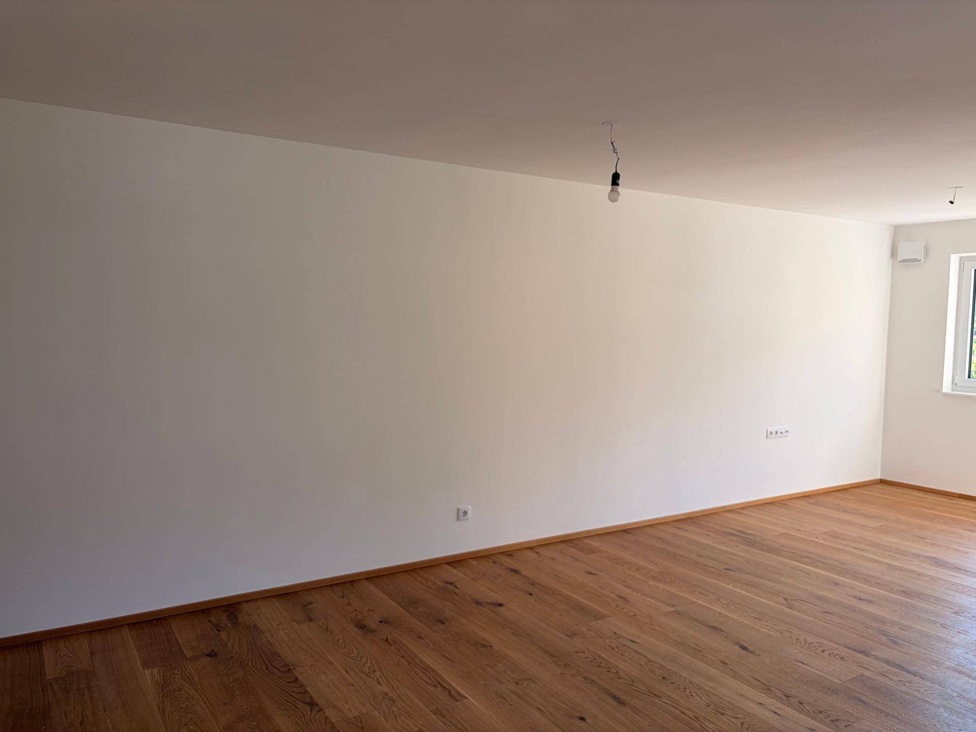 Heller Wohnbereich mit Holzboden, weißen Wänden und ausreichend Steckdosen.