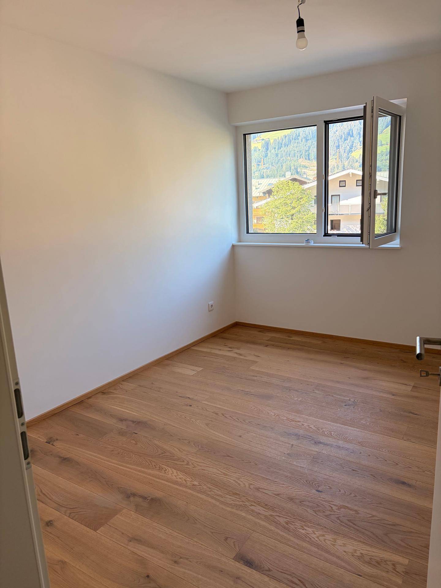 Schlafzimmer mit Holzboden, weiß gestrichenen Wänden und Bergblick durch das Fenster.