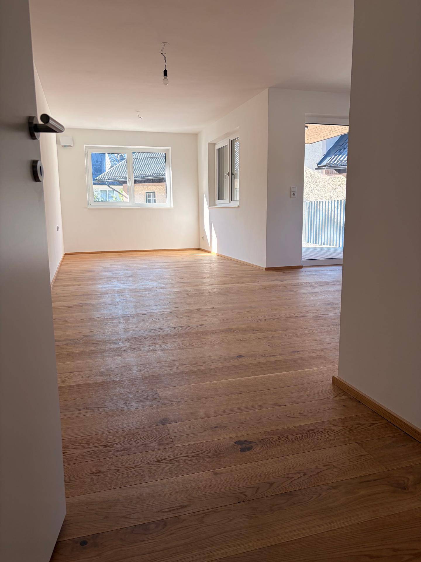 Lichtdurchfluteter Wohnbereich mit Holzboden und Zugang zum sonnigen Balkon.