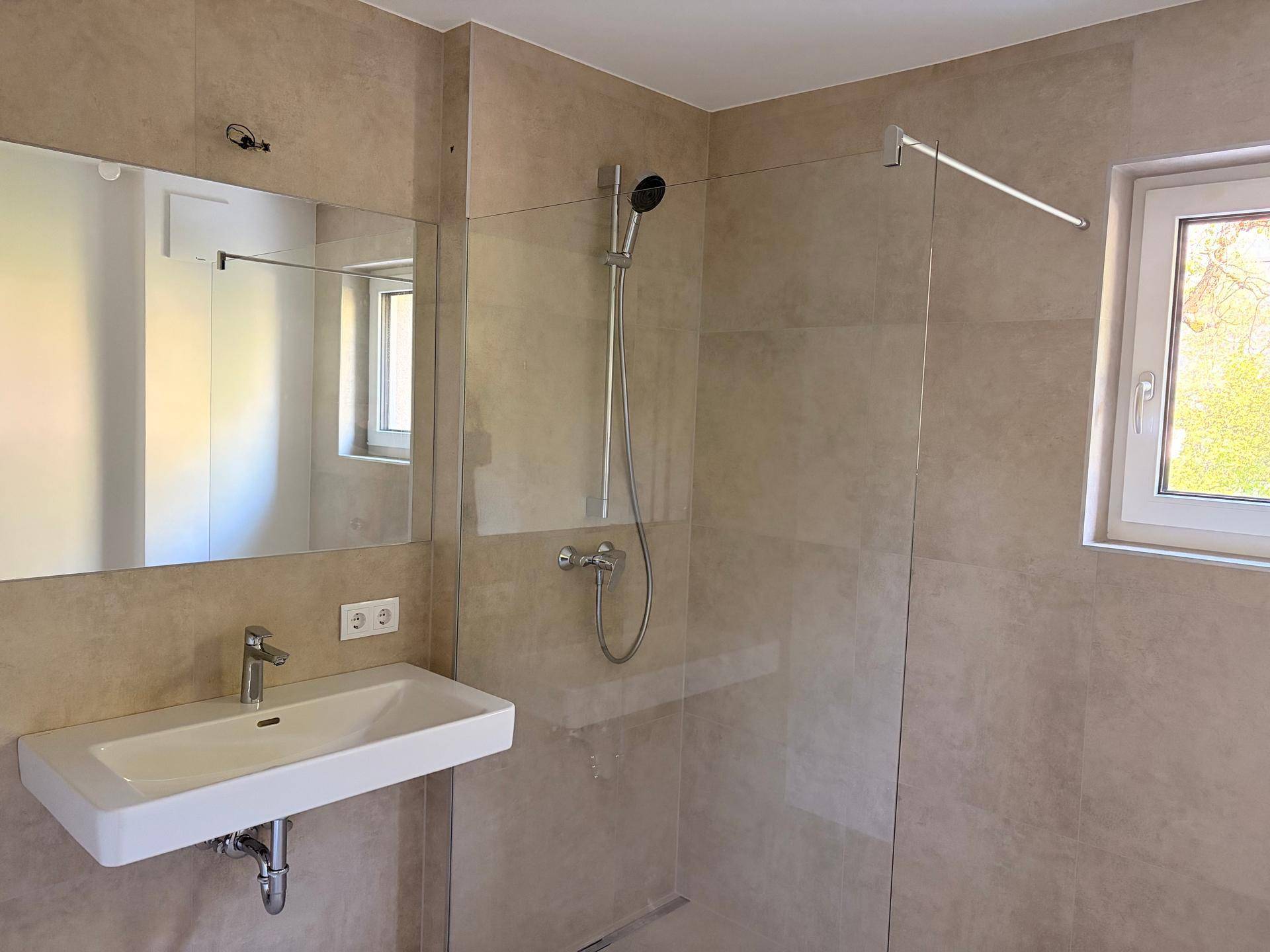 Helles Badezimmer mit großer Glasdusche, modernem Waschbecken und Fenster.