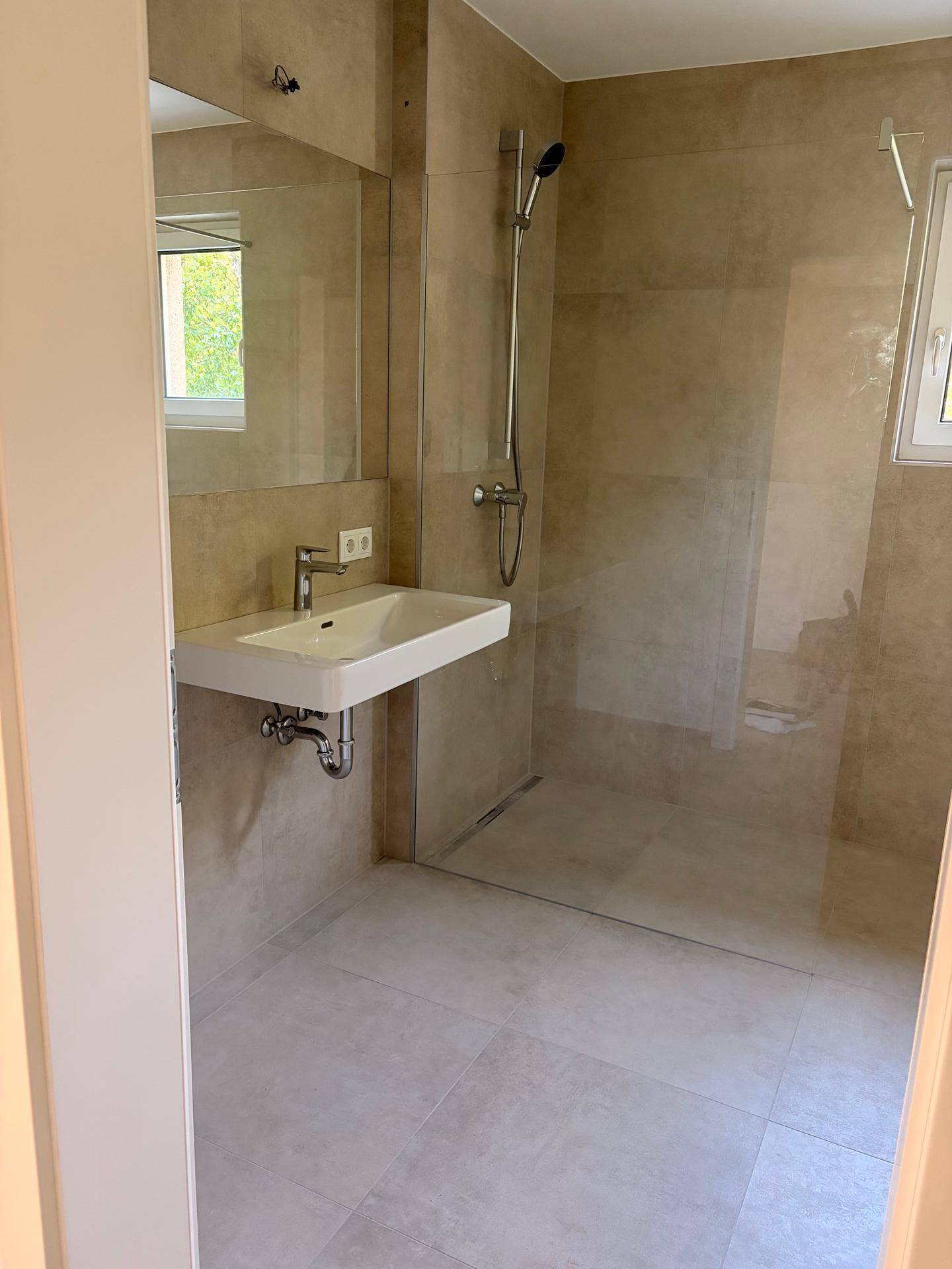 Modernes Badezimmer mit ebenerdiger Dusche, Waschbecken und hellen Fliesen.