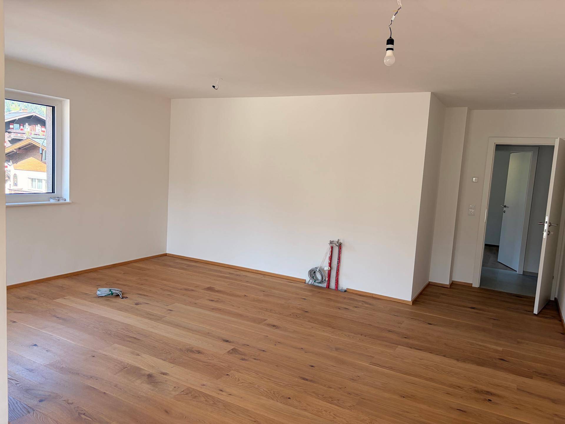 Geräumiger Wohnbereich mit Holzboden und vorbereiteten Anschlüssen für eine Küche.