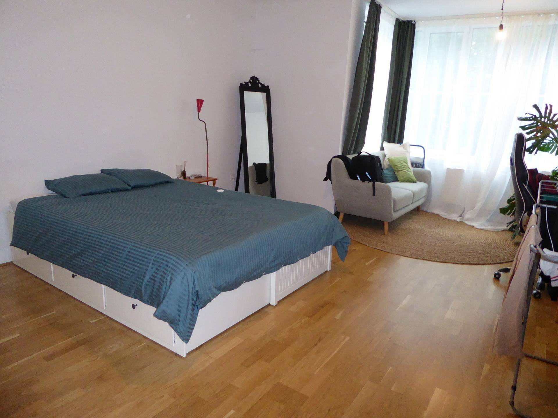 Schlafzimmer mit Doppelbett, Sofa, großem Spiegel und hellem Fensterbereich.