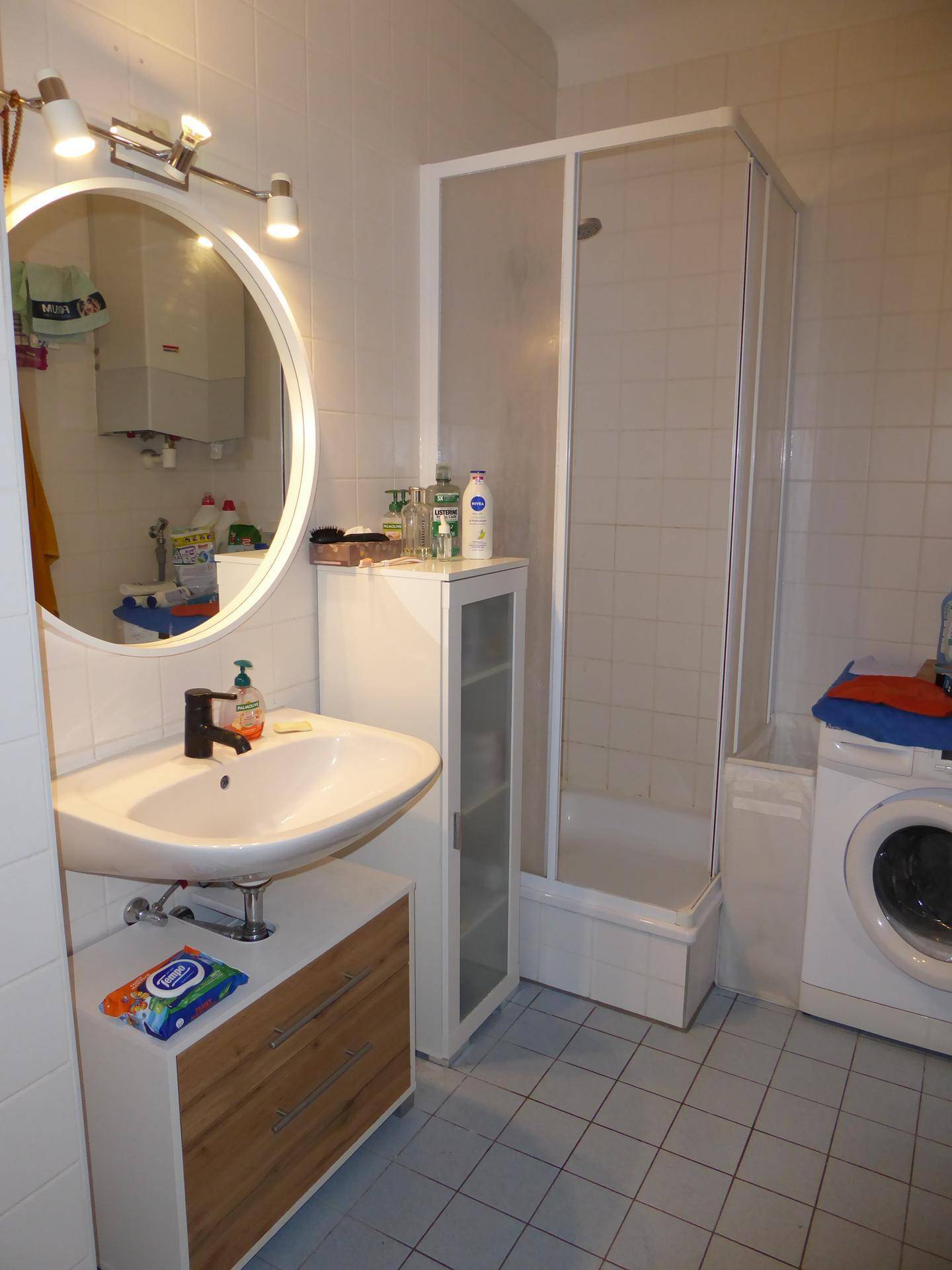 Badezimmer mit Waschbecken, Duschkabine und Waschmaschine, funktional eingerichtet.