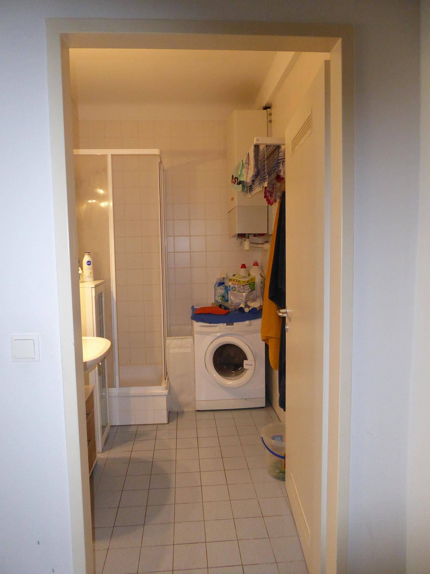 Blick in das Badezimmer mit Duschkabine, Waschbecken und Waschmaschine.