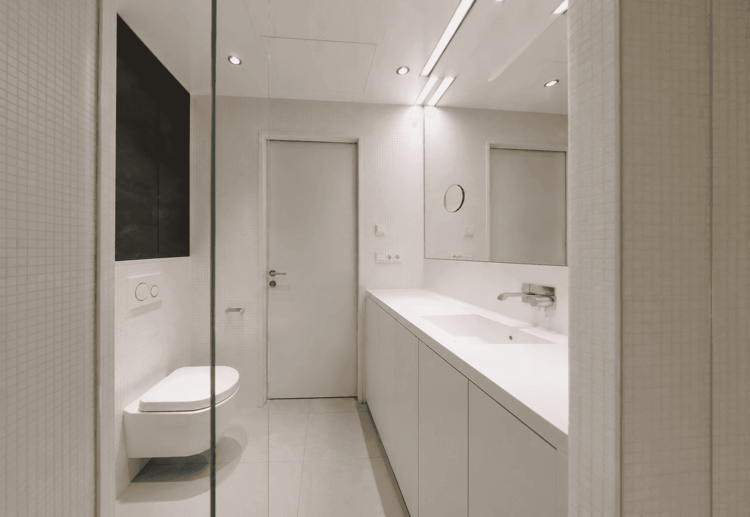 Modernes Badezimmer mit weißen Mosaikfliesen, wandhängendem WC und großem Waschtisch.