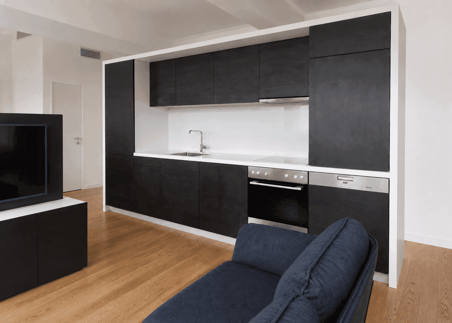 Moderne schwarze Einbauküche mit integrierten Geräten und Holzboden in offenem Wohnbereich.