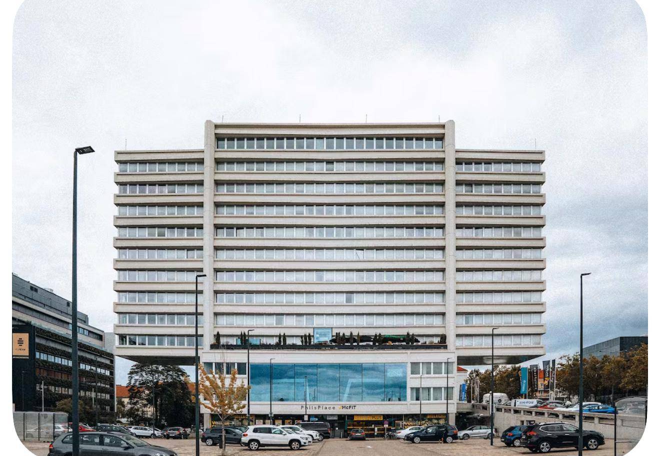Großes modernes Gebäude mit vielen Fenstern und einem Parkplatz davor.