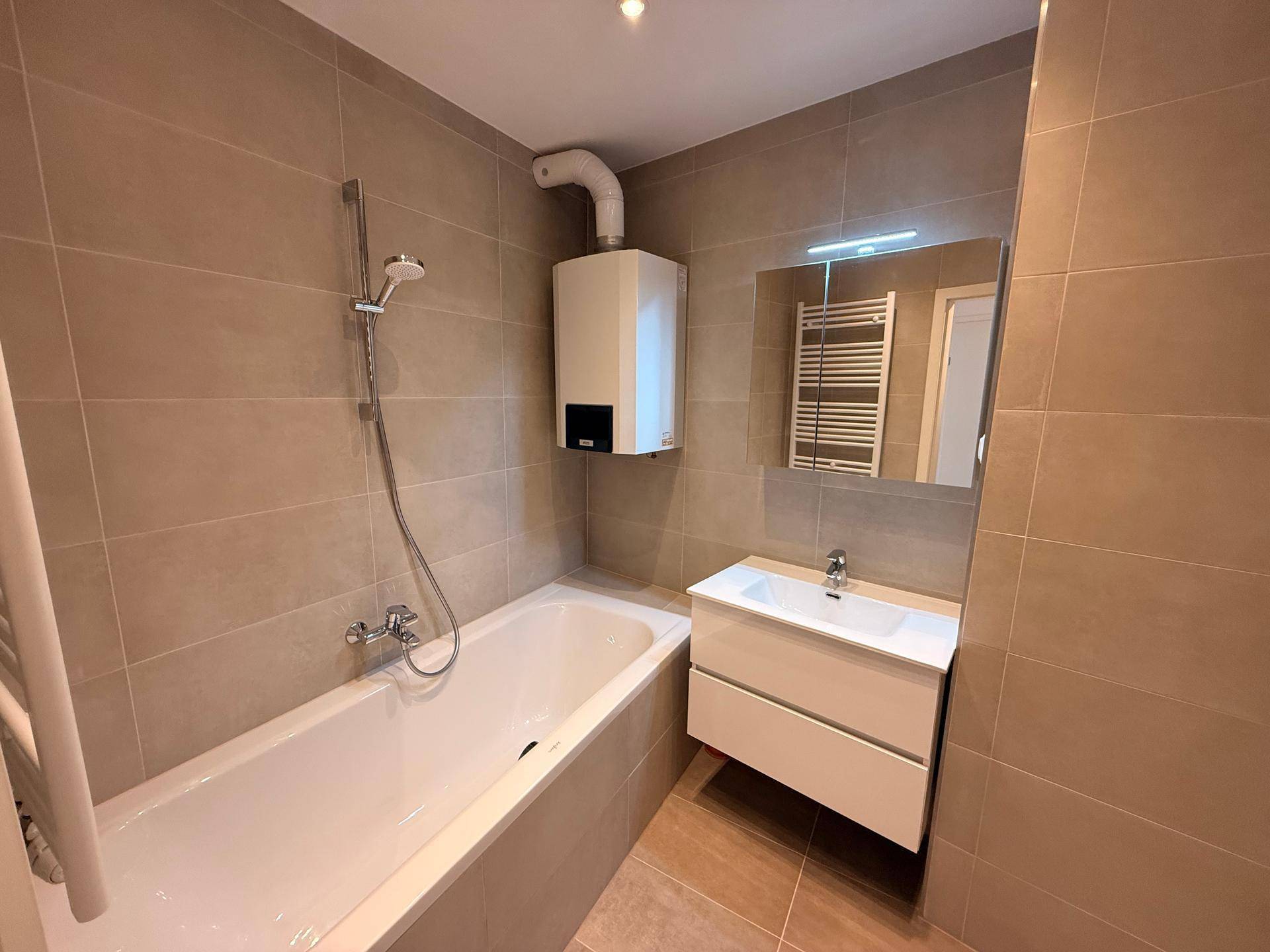 Badezimmer mit Badewanne, Waschtisch und Heizkörper, alles in neutralen Farbtönen gehalten.