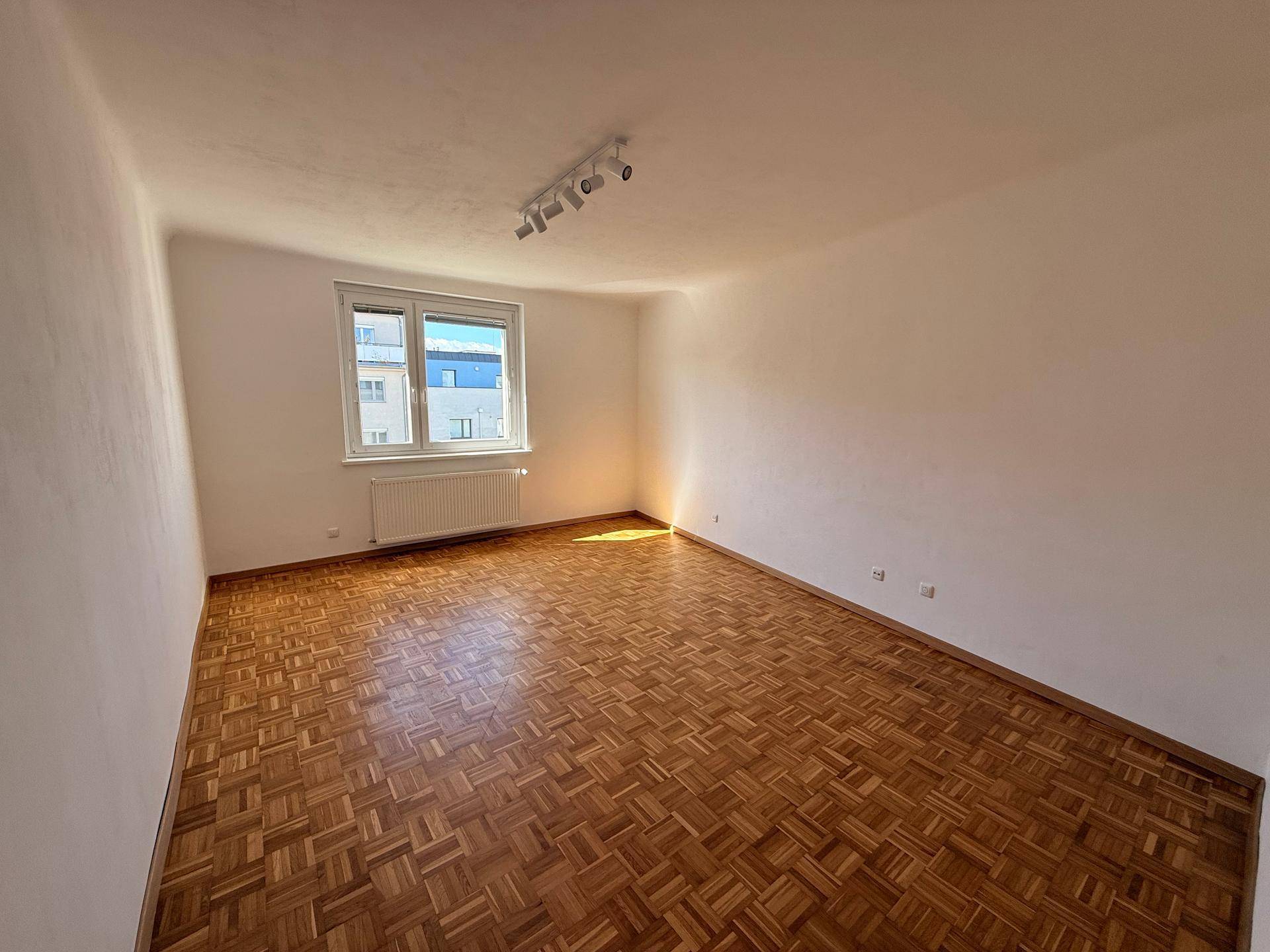 Großes, helles Wohnzimmer mit Parkettboden und Blick auf die umliegenden Gebäude.