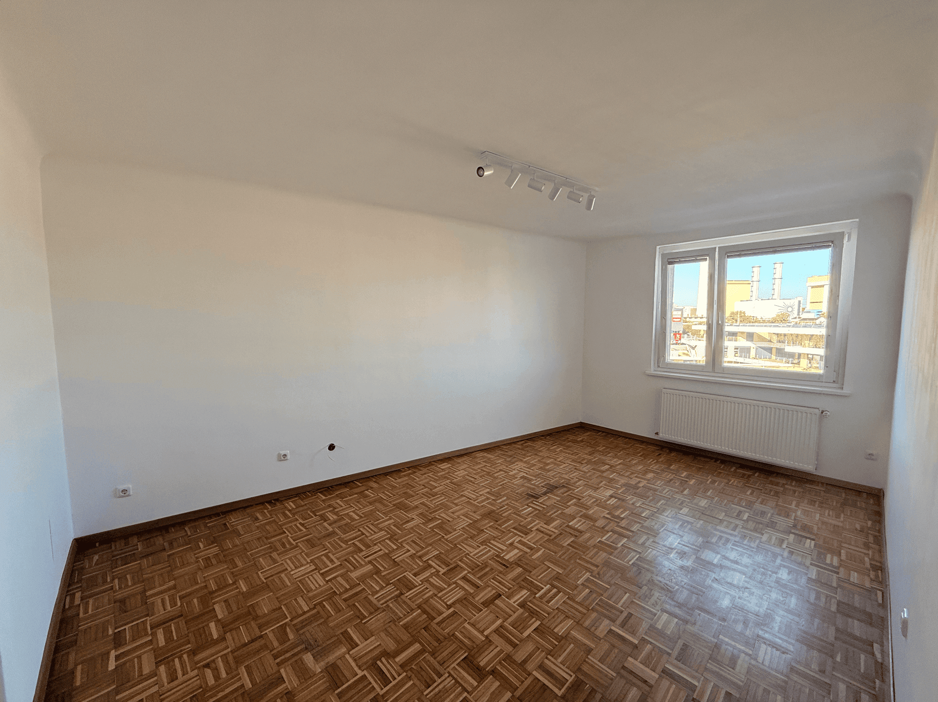 Geräumiges Wohnzimmer mit Parkettboden und großem Fenster, das viel Tageslicht hereinlässt.