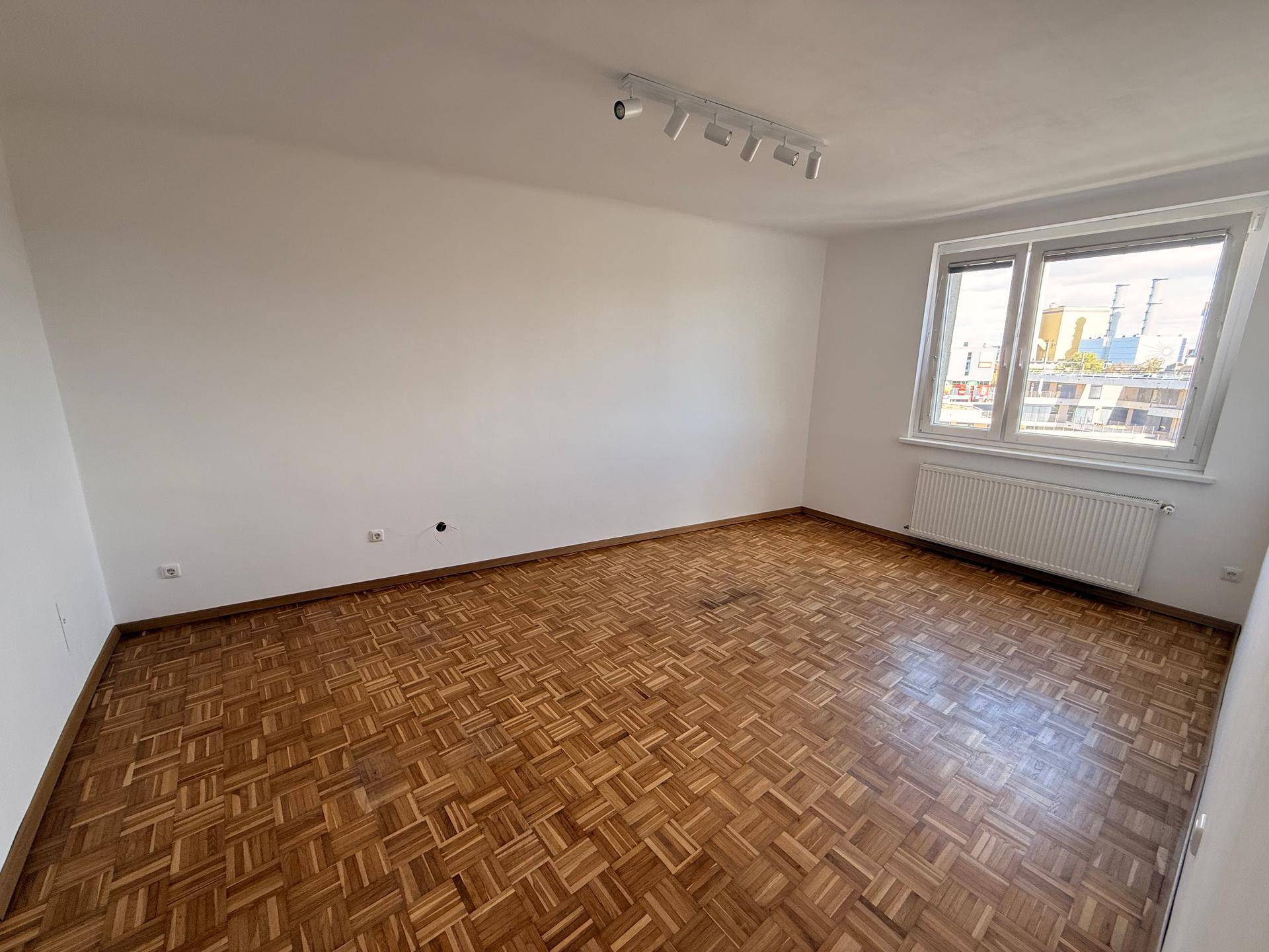 Geräumiges Wohnzimmer mit Parkettboden und großem Fenster für natürliche Belichtung.