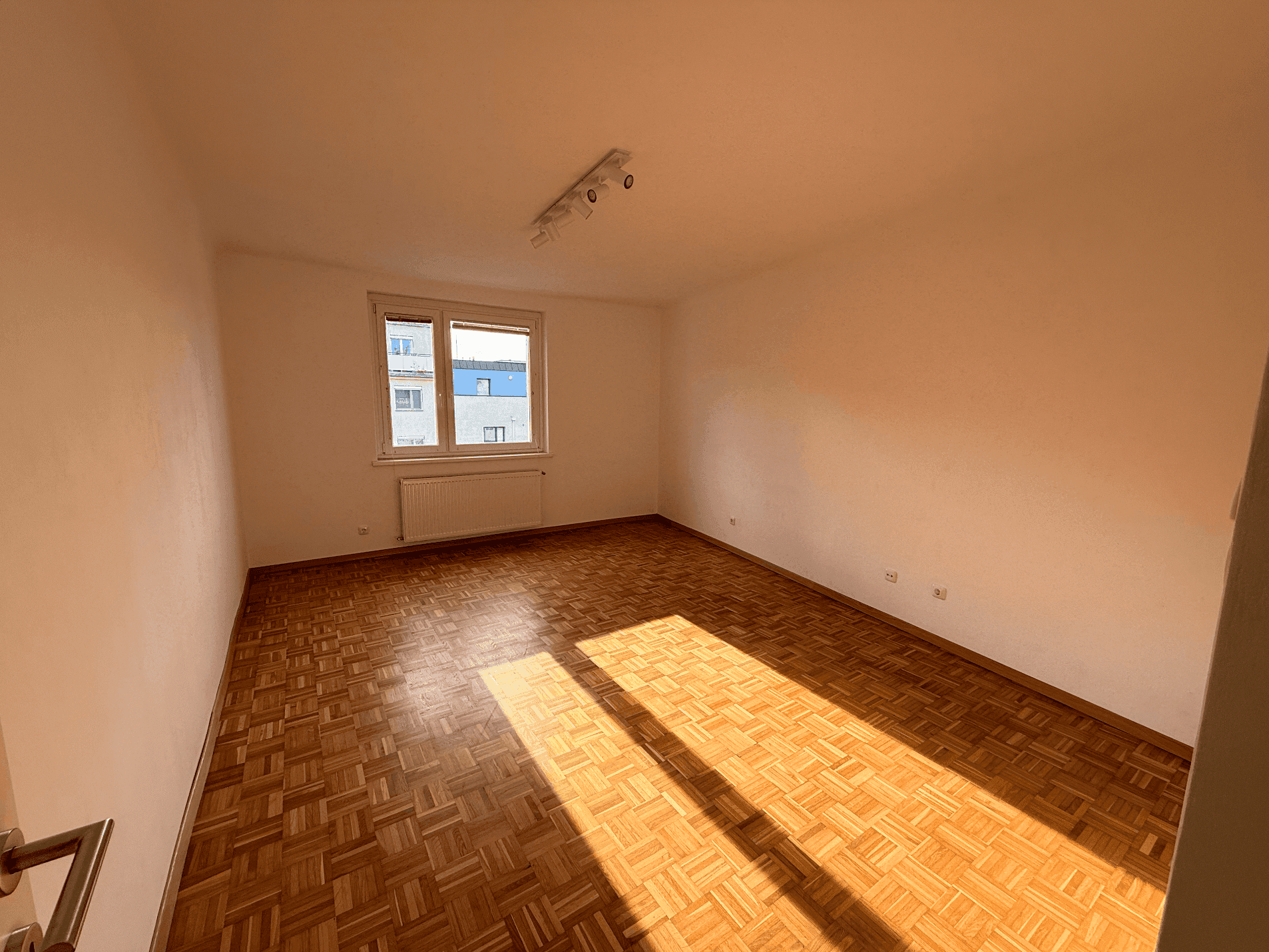 Lichtdurchflutetes Wohnzimmer mit Parkettboden und sonnigem Ausblick durch das Fenster.