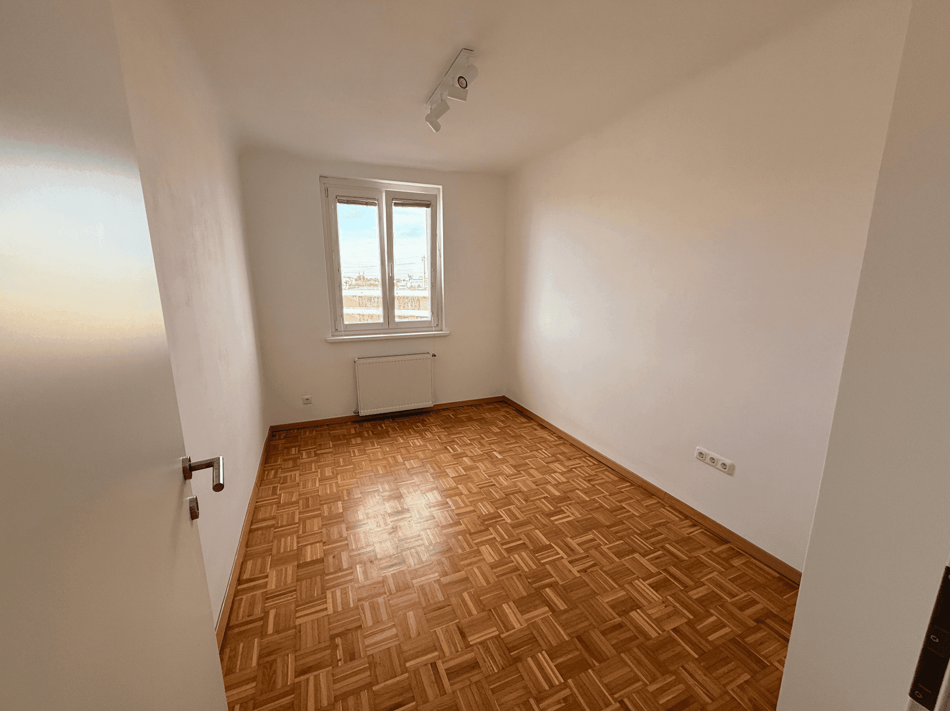 Helles Zimmer mit Parkettboden und Fenster, bereit zur individuellen Gestaltung.