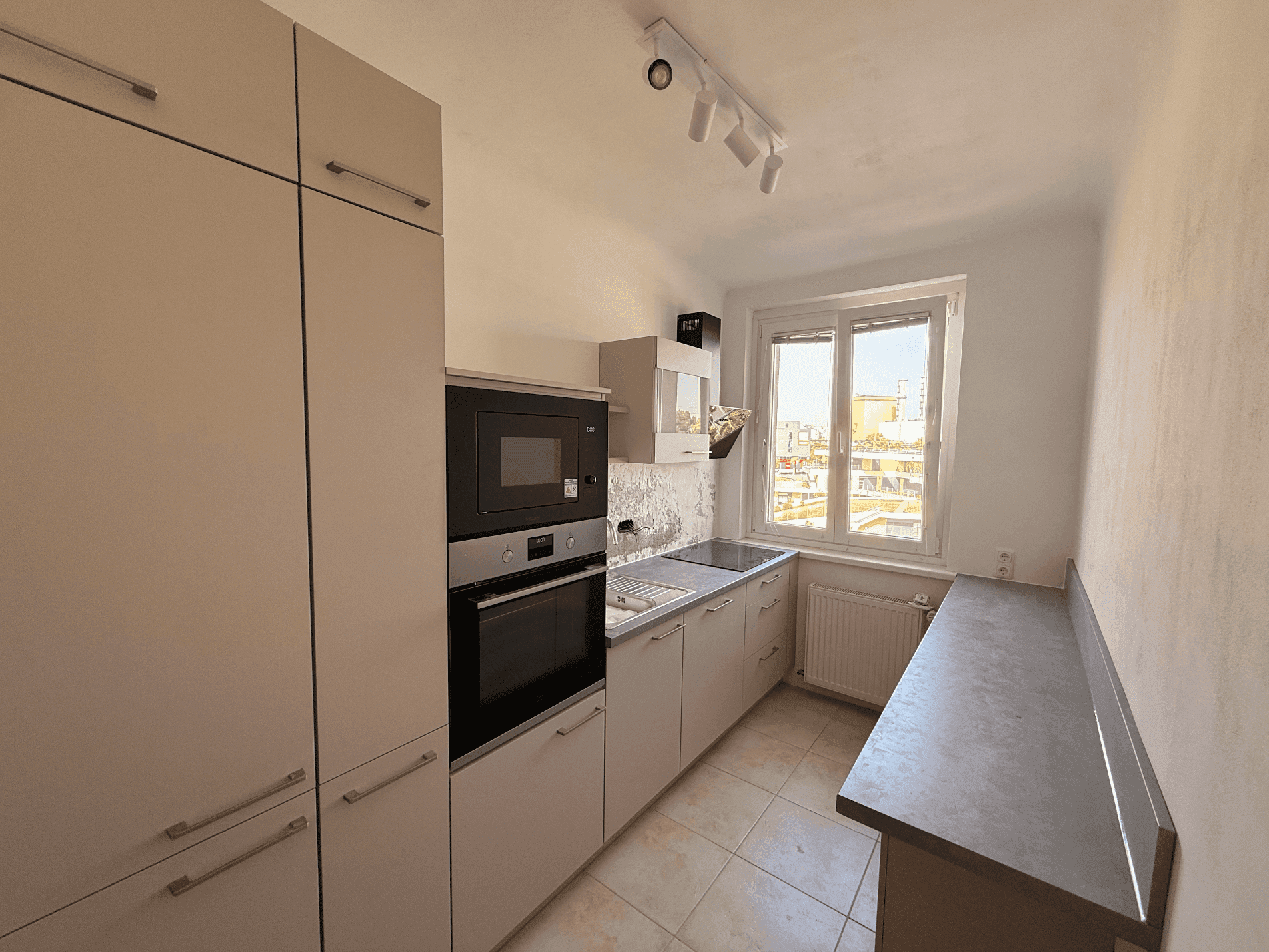 Funktionale Küche mit hellen Schränken, integrierten Geräten und Fenster mit Stadtblick.