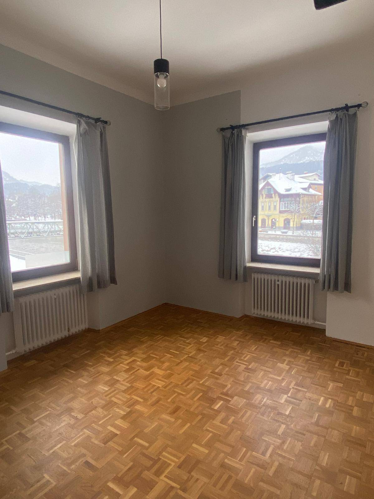 Geräumiges Zimmer mit Parkettboden und zwei Fenstern, die einen Blick auf die verschneite Landschaft bieten.