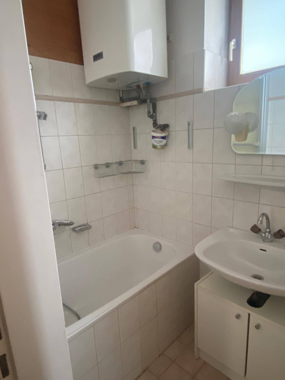 Kleines Badezimmer mit Badewanne, Waschbecken und weißen Fliesen, funktional eingerichtet.