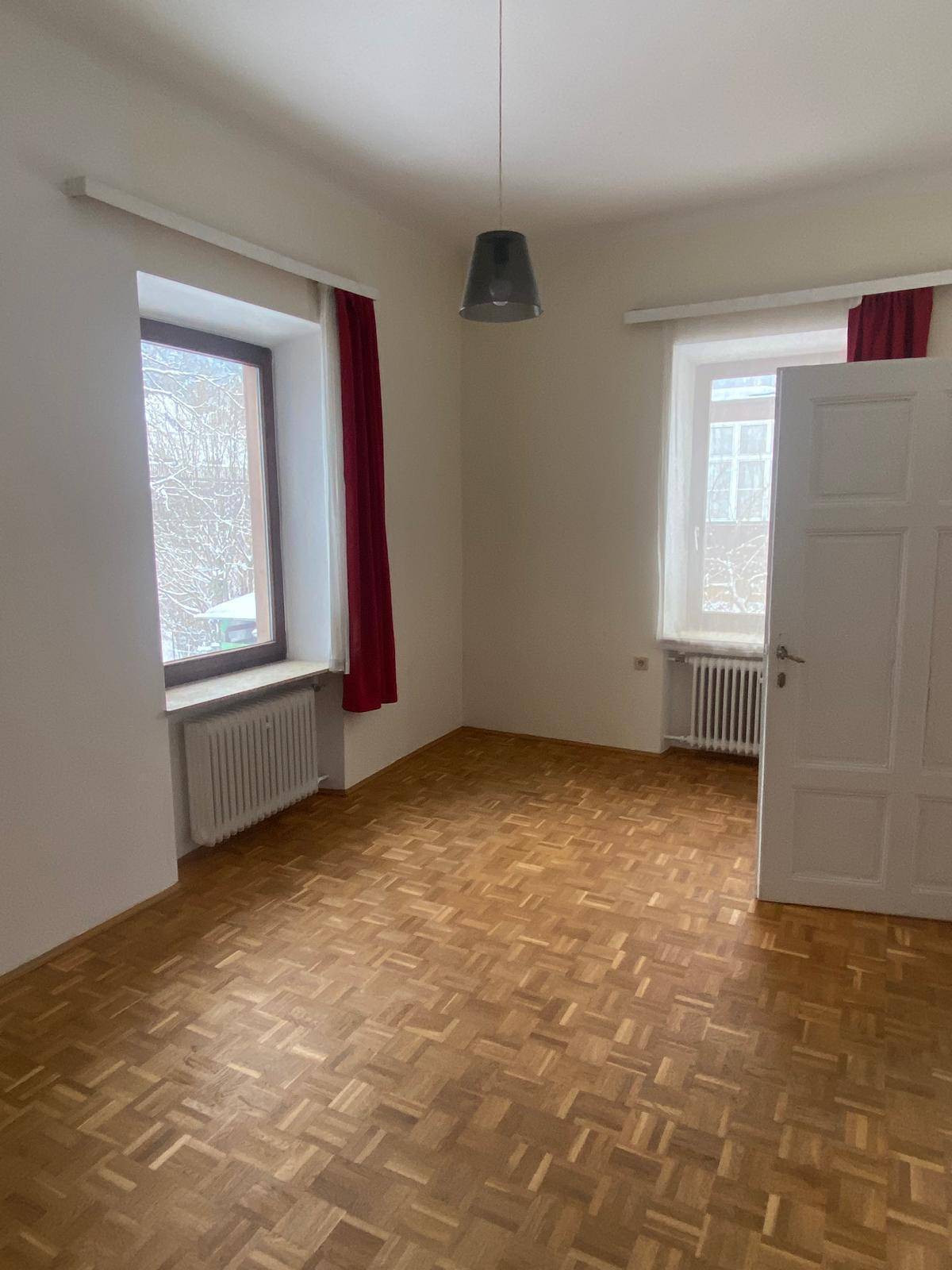Helles Zimmer mit Parkettboden und zwei Fenstern, die für gute Belichtung sorgen.