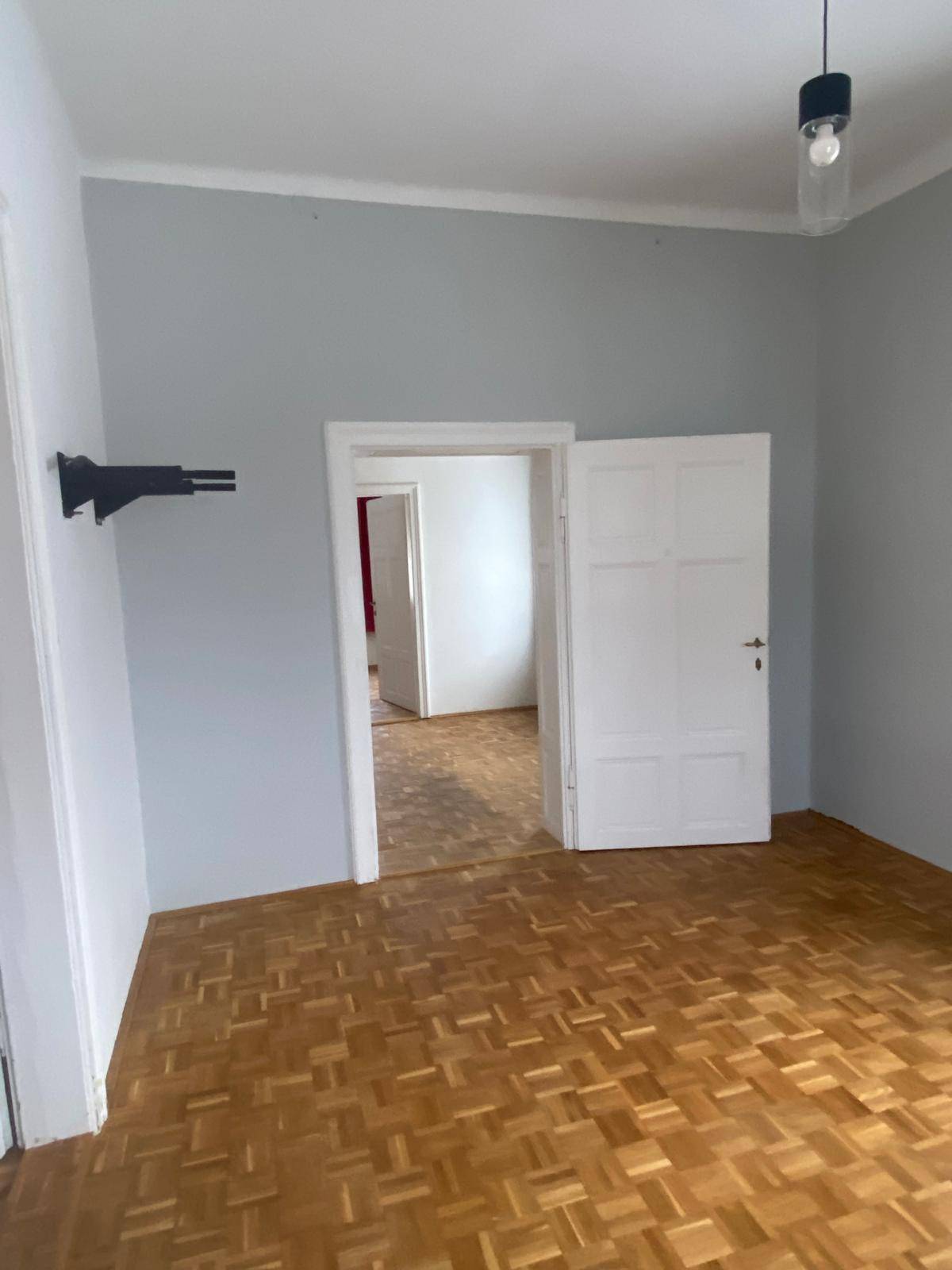 Leeres Zimmer mit Parkettboden und hellblauen Wänden, bereit zur individuellen Gestaltung.