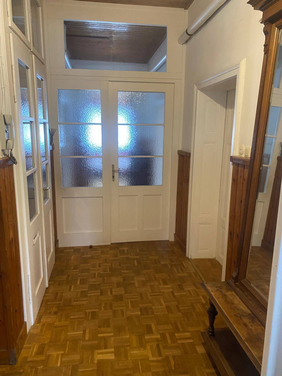 Heller Eingangsbereich mit Parkettboden, Holzvertäfelung und traditionellen Glastüren.