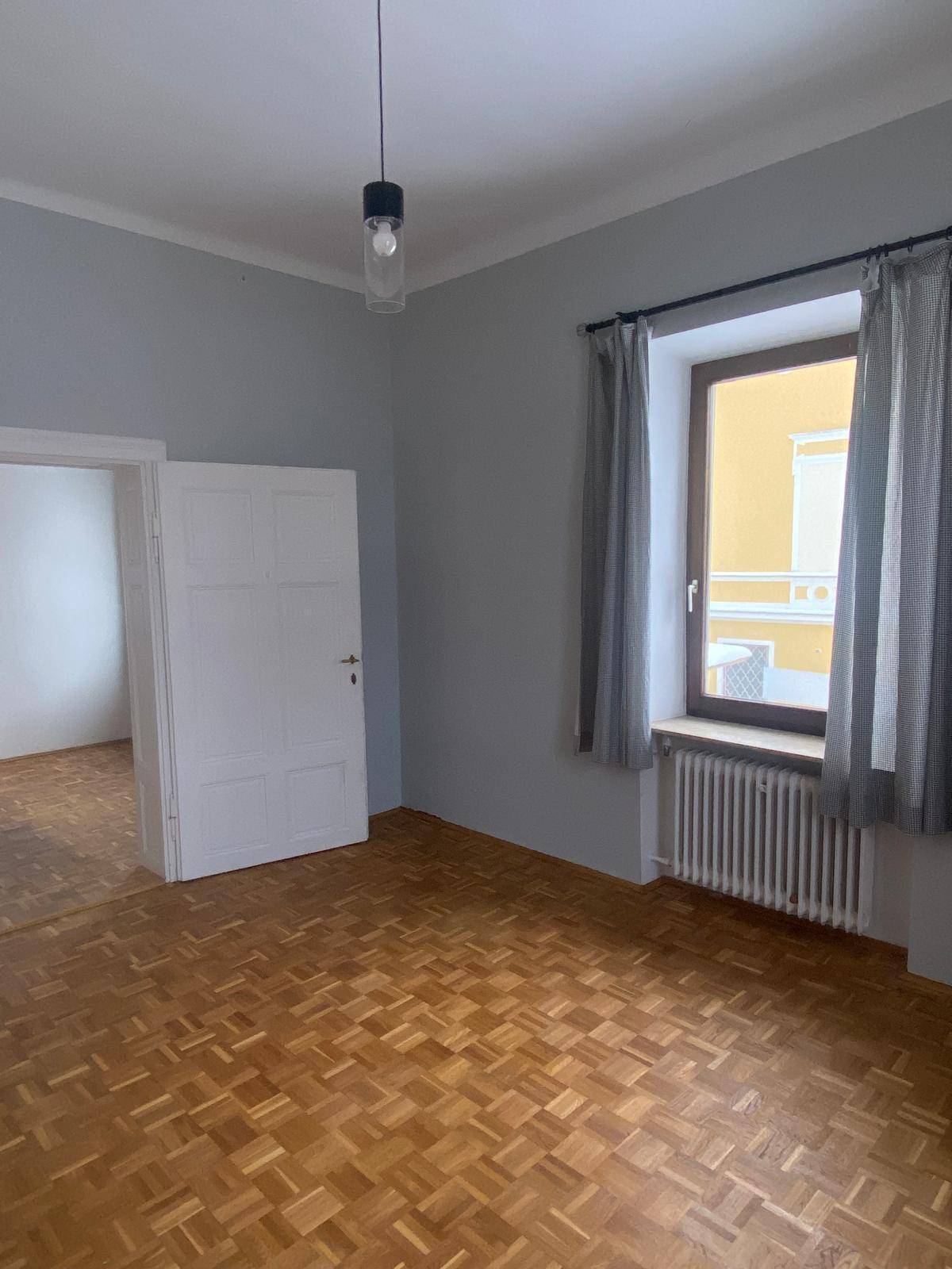 Helles Zimmer mit Parkettboden, hellblauen Wänden und einem Fenster mit Blick nach draußen.