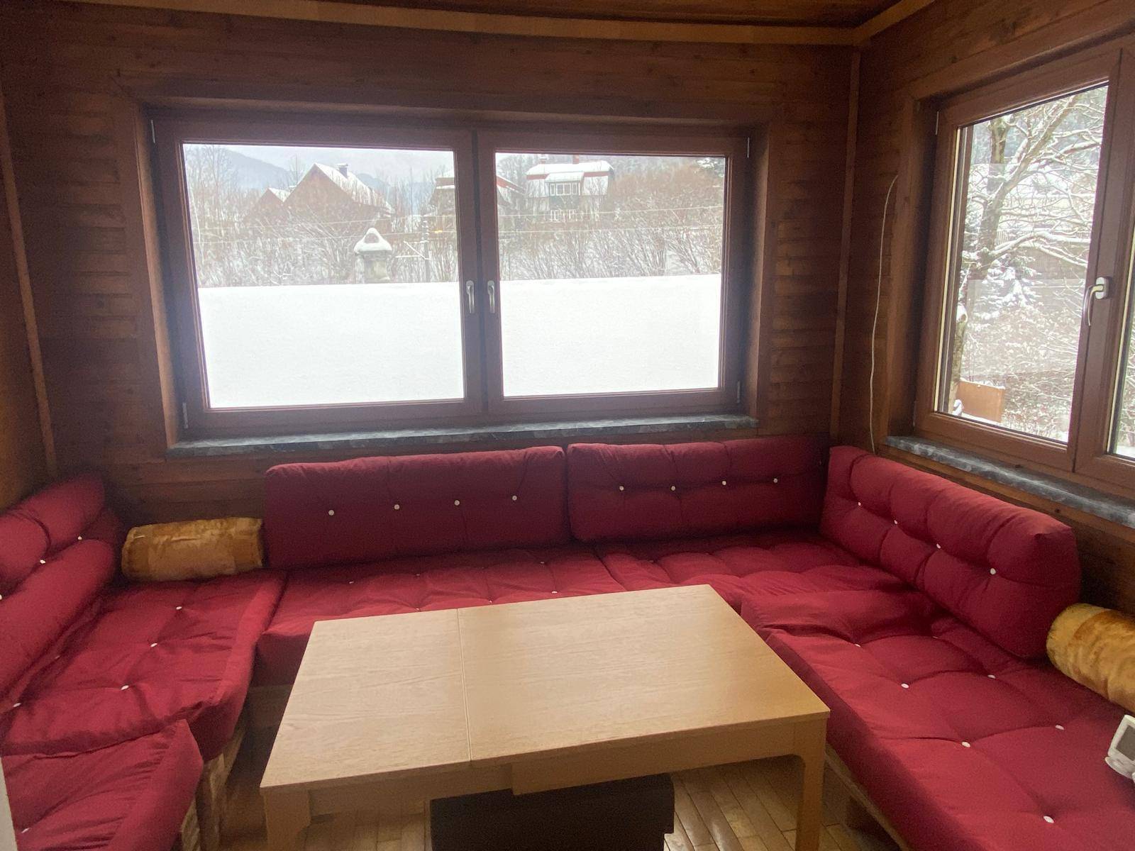 Gemütlicher Wintergarten mit Holzwänden, roten Sitzpolstern und Blick auf die verschneite Umgebung.