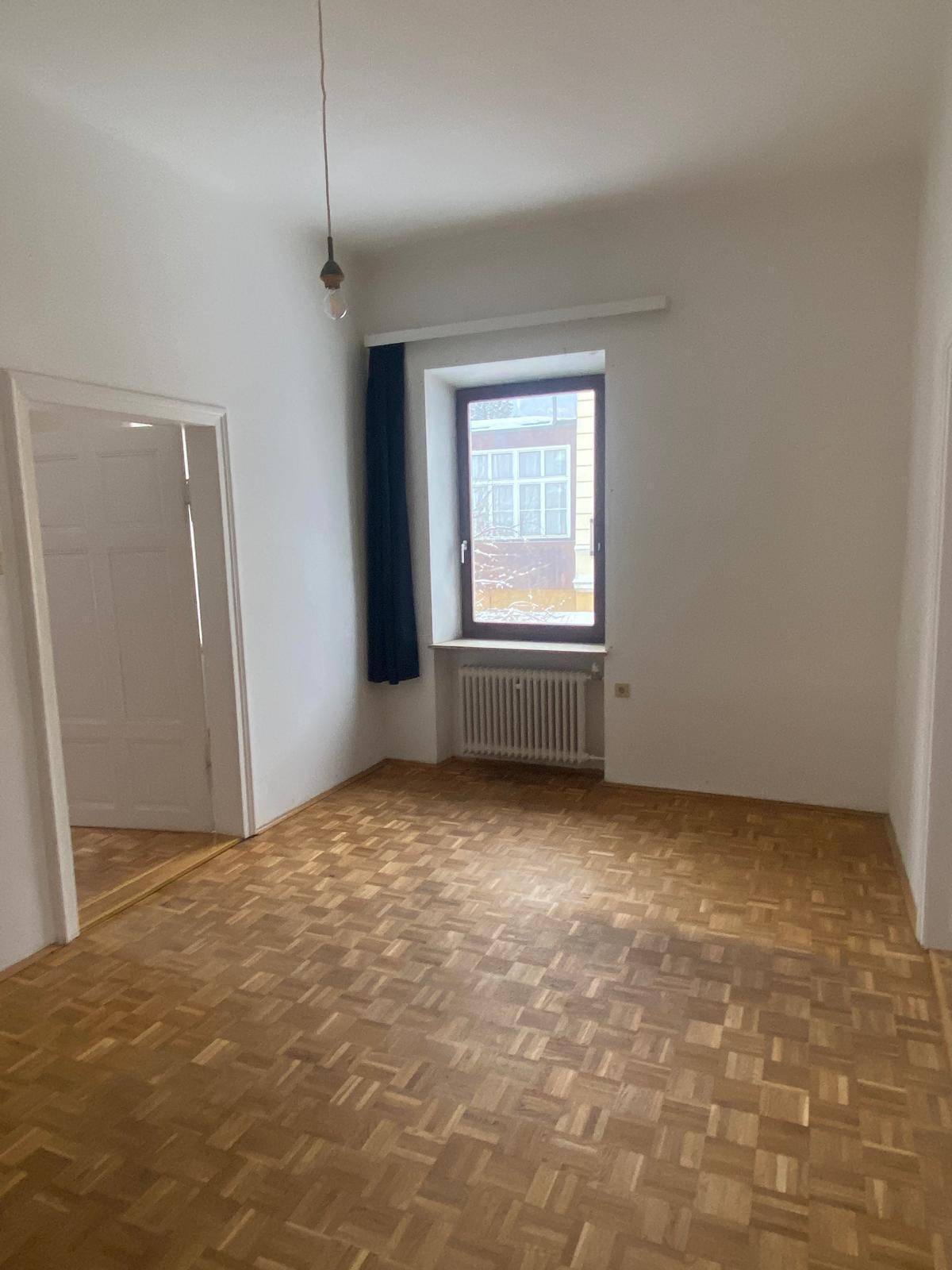 Helles Zimmer mit Parkettboden und einem Fenster, das viel Tageslicht hereinlässt.