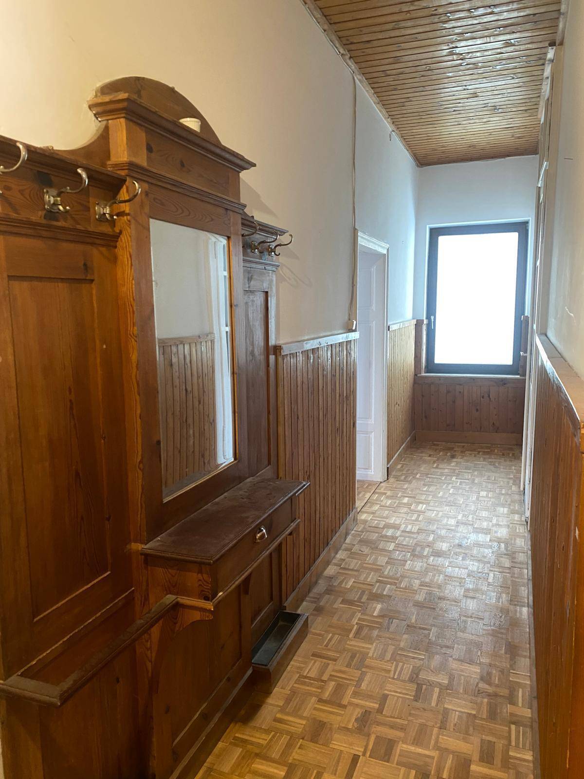 Langer Flur mit Holzparkett, Holzvertäfelung und einem traditionellen Garderobenschrank mit Spiegel.