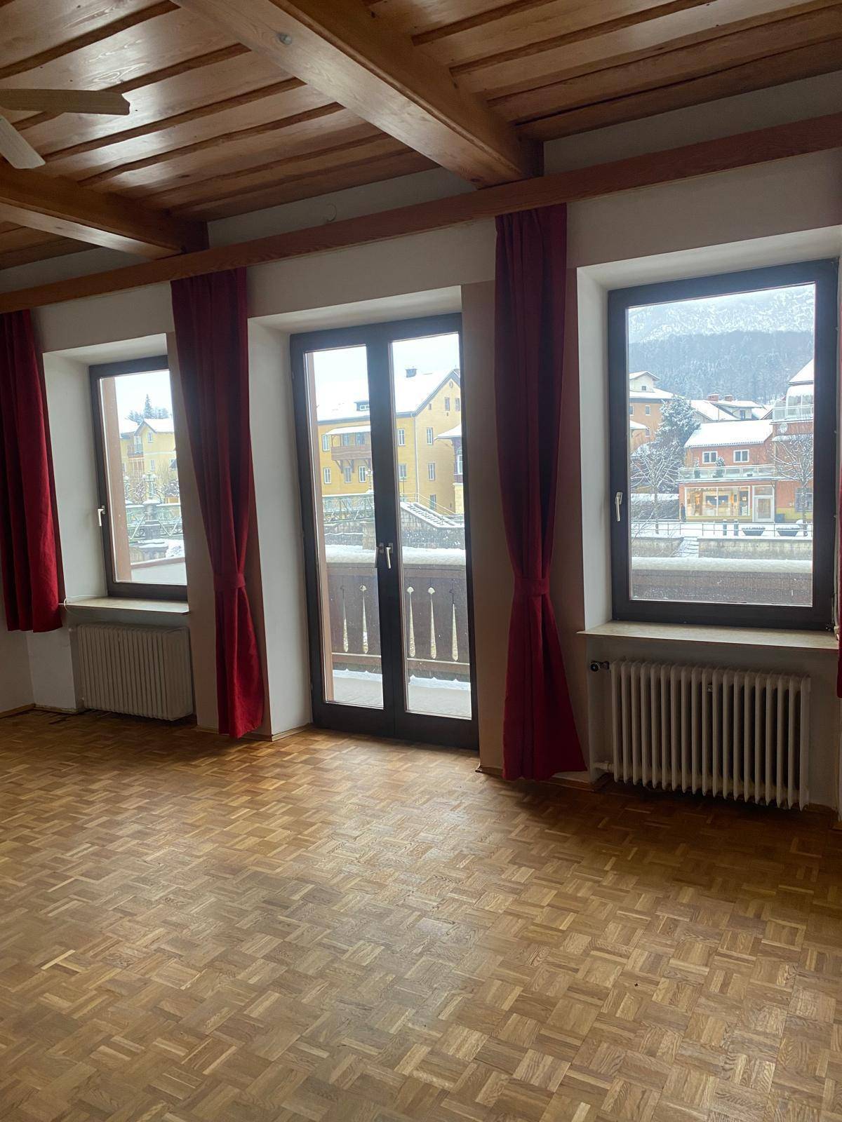 Geräumiges Zimmer mit Holzbalkendecke, Parkettboden und Zugang zu einem kleinen Balkon.