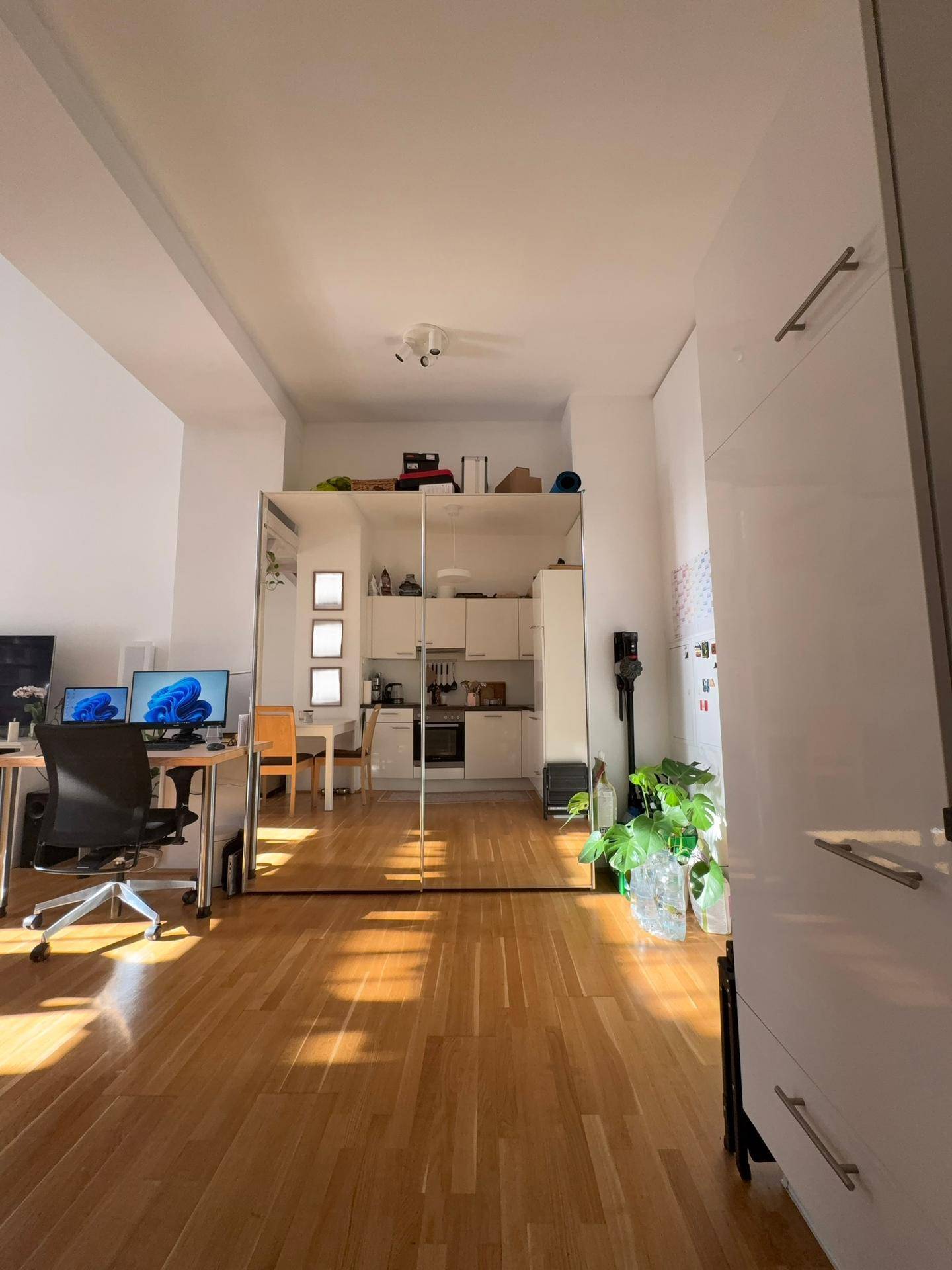 Heller Raum mit Arbeitsplatz und Spiegelschrank, der die moderne Küche reflektiert.